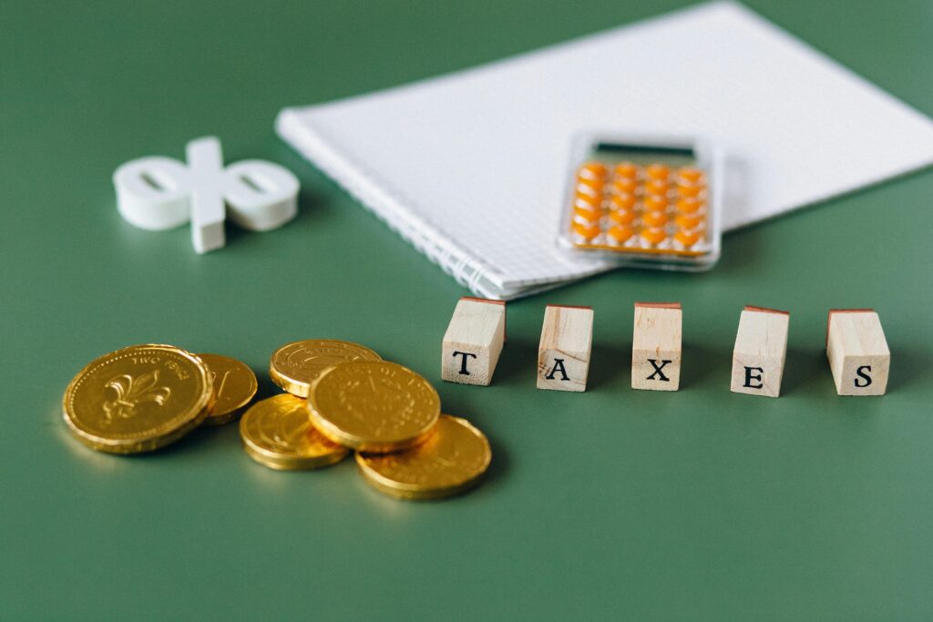 pexels photo 6863191 6863191 Close-up of tax-related items including coins, calculator, and word 'taxes' on a green background.