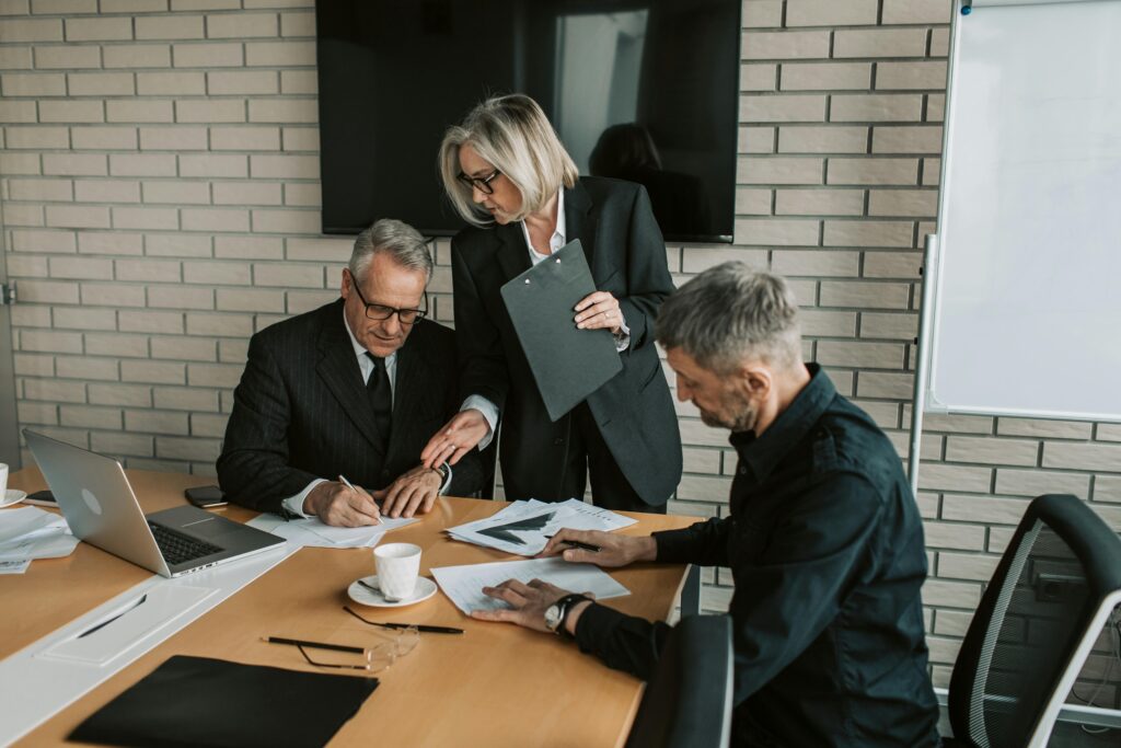 pexels photo 7433919 7433919 Three mature professionals in a business meeting discussing and signing documents in an office setting.
