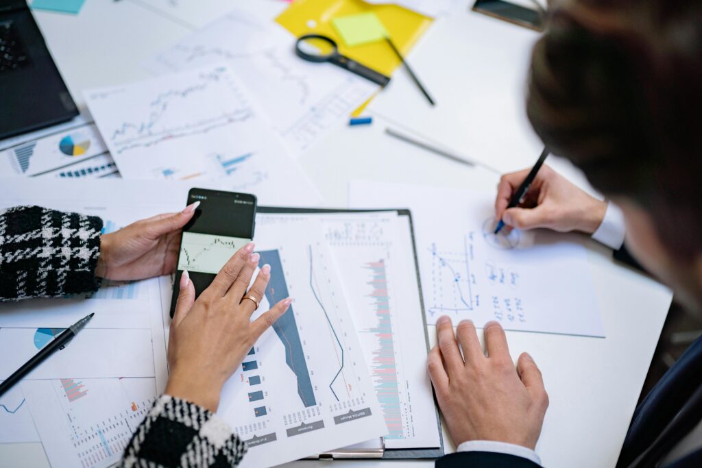 pexels photo 7693744 7693744 Overhead view of people analyzing financial graphs and data with smartphone and documents.